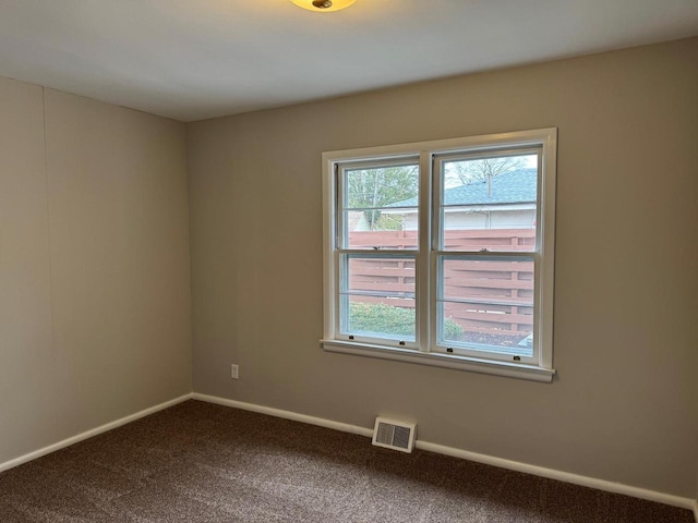 spare room with dark colored carpet, visible vents, and baseboards