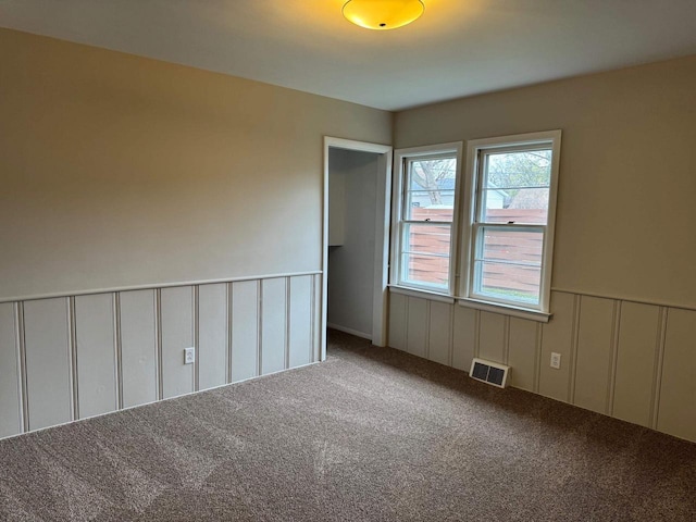spare room with a wainscoted wall, visible vents, carpet flooring, and a decorative wall