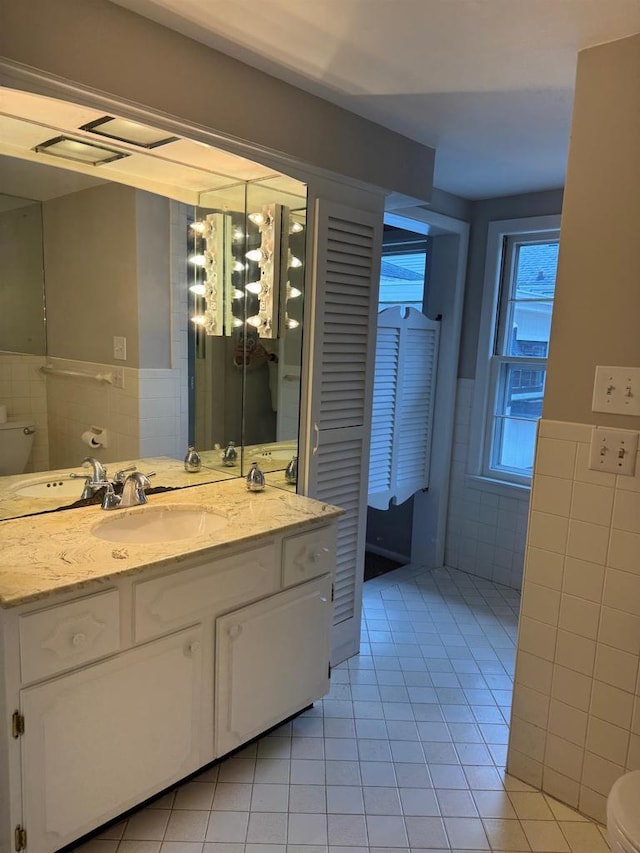 bathroom featuring toilet, a wainscoted wall, tile patterned floors, and tile walls