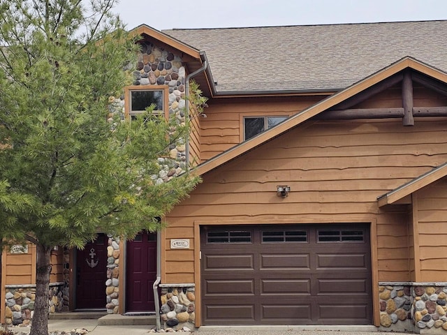 view of front of house with an attached garage, roof with shingles, and stone siding