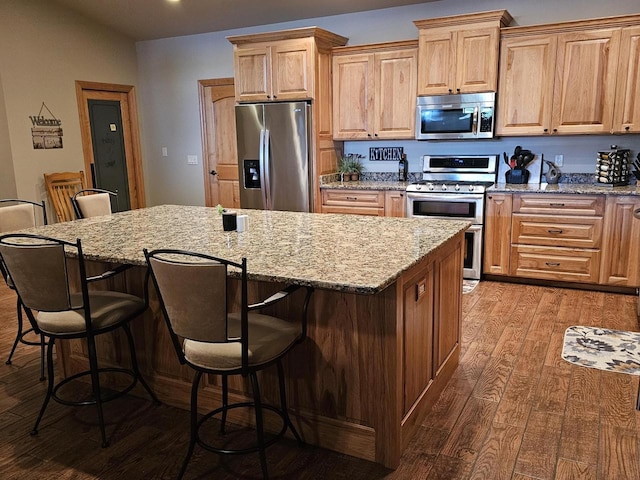 kitchen featuring light stone countertops, wood finished floors, a kitchen island, and appliances with stainless steel finishes