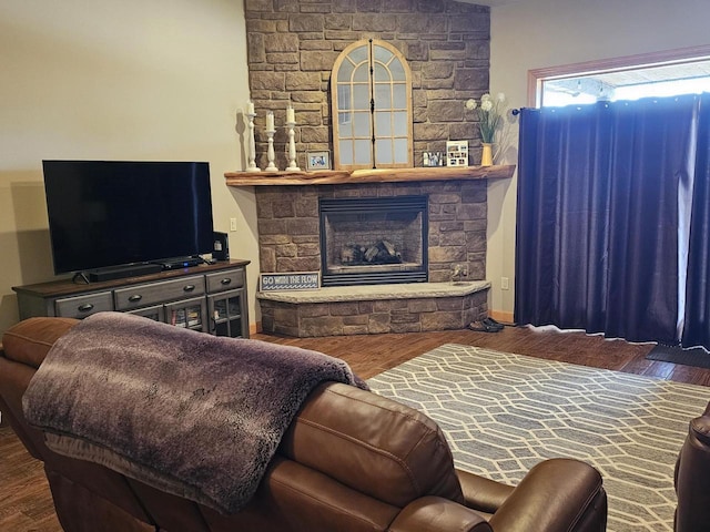 living area featuring baseboards, a stone fireplace, and wood finished floors