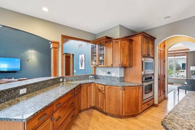 1310 Hanover Ct, Waunakee, WI 53597 - kitchen featuring stainless steel appliances, stone countertops, arched walkways, and brown cabinets