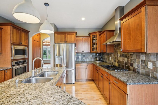 1310 Hanover Ct, Waunakee, WI 53597 - kitchen featuring light wood finished floors, a sink, wall chimney range hood, light stone countertops, and appliances with stainless steel finishes