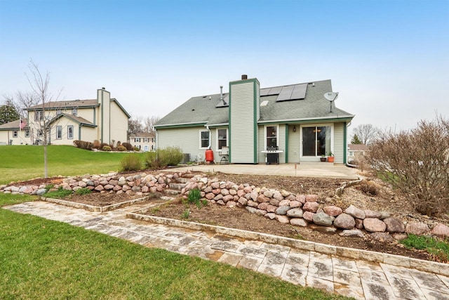 rear view of property with solar panels, a lawn, a chimney, and a patio