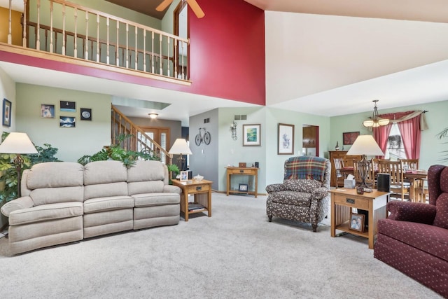 carpeted living area with stairway, visible vents, a towering ceiling, and a ceiling fan