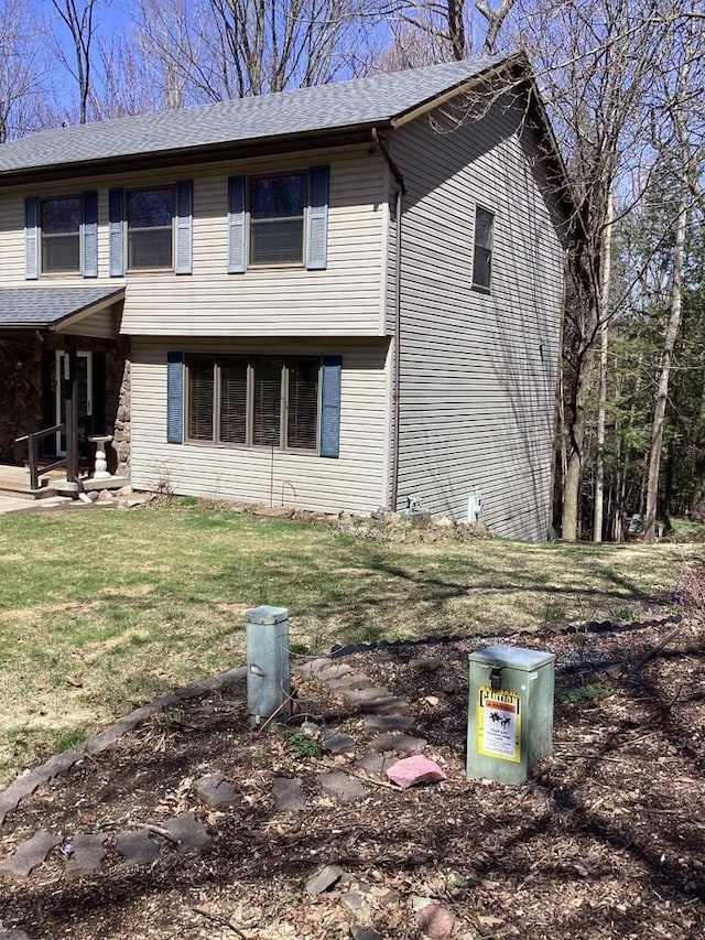 view of side of property with roof with shingles and a yard