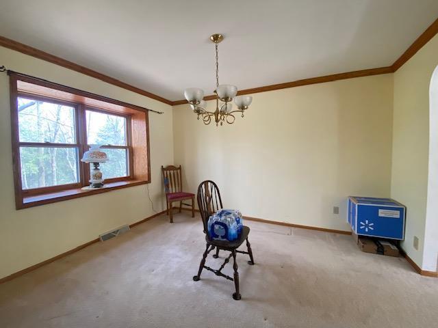 unfurnished room with visible vents, crown molding, baseboards, an inviting chandelier, and carpet