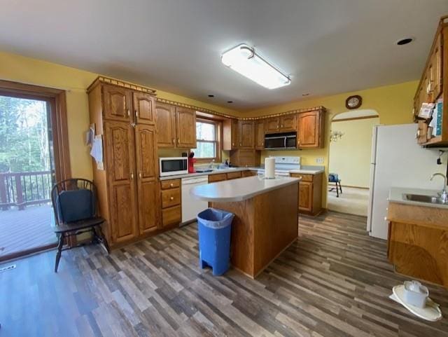 kitchen featuring brown cabinetry, white appliances, a center island, light countertops, and dark wood finished floors