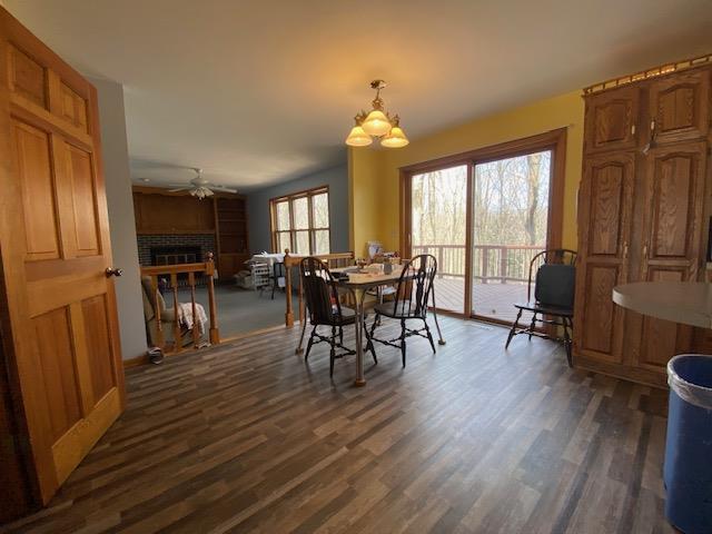 dining area with dark wood-type flooring, ceiling fan with notable chandelier, and a tile fireplace