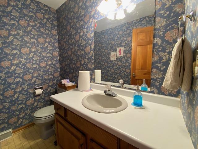 half bath with visible vents, tile patterned flooring, vanity, toilet, and baseboards