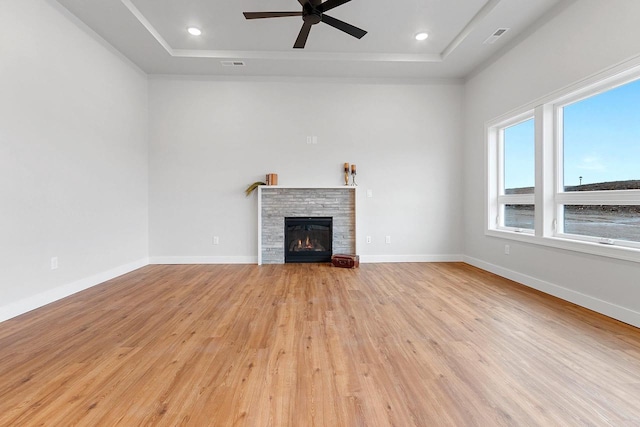 unfurnished living room featuring a raised ceiling, light wood-type flooring, a ceiling fan, and a stone fireplace