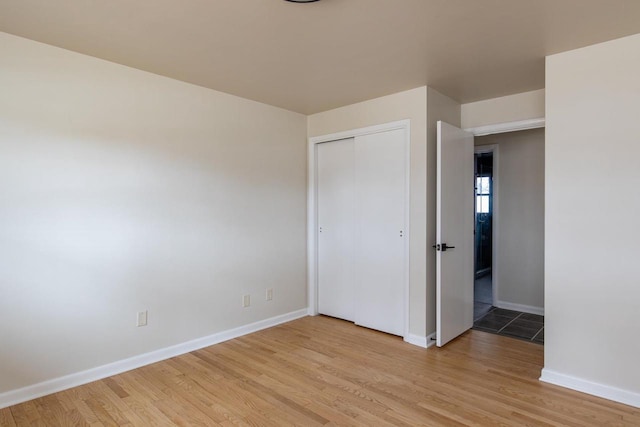 unfurnished bedroom with baseboards, light wood-style floors, and a closet