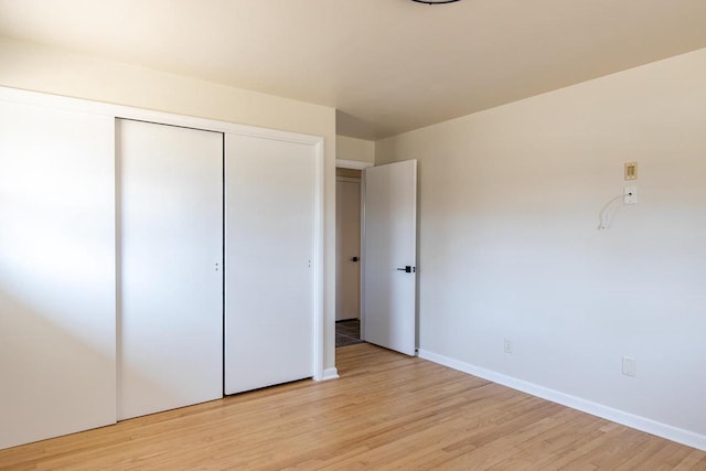 unfurnished bedroom featuring light wood-style flooring, baseboards, and a closet