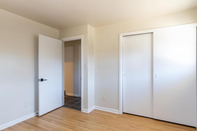unfurnished bedroom featuring baseboards, a closet, and light wood-type flooring