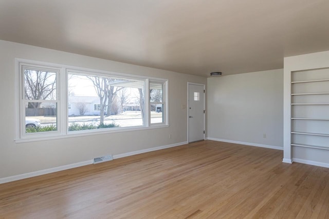 unfurnished living room featuring light wood-style flooring, visible vents, built in features, and baseboards