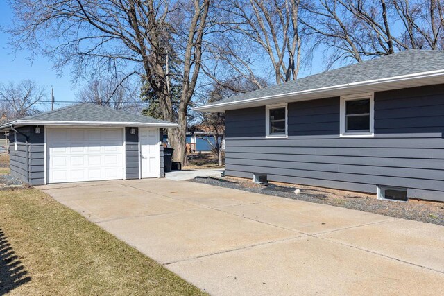 view of side of property featuring concrete driveway, an outbuilding, a detached garage, and a shingled roof
