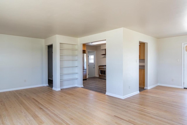 unfurnished living room with baseboards, light wood finished floors, and built in shelves