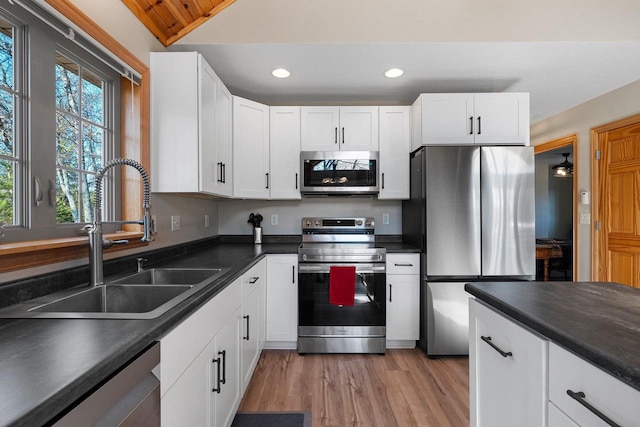 kitchen with a sink, dark countertops, recessed lighting, white cabinetry, and appliances with stainless steel finishes