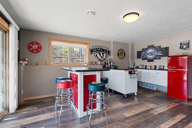 bar featuring freestanding refrigerator, visible vents, a bar, and dark wood-style flooring