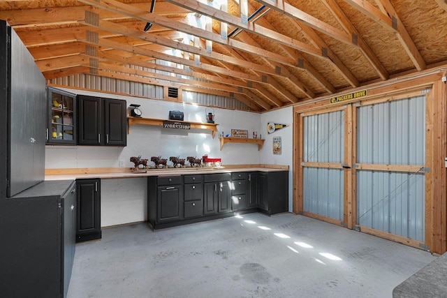 kitchen featuring concrete flooring, vaulted ceiling, dark cabinets, and open shelves