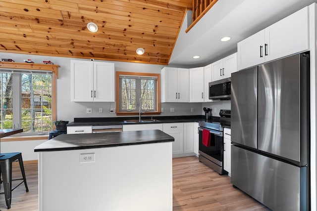 kitchen with dark countertops, vaulted ceiling, a sink, light wood-type flooring, and appliances with stainless steel finishes