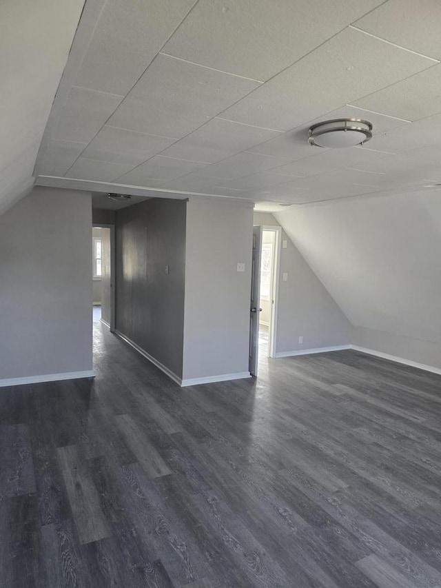 bonus room with dark wood finished floors, vaulted ceiling, and baseboards