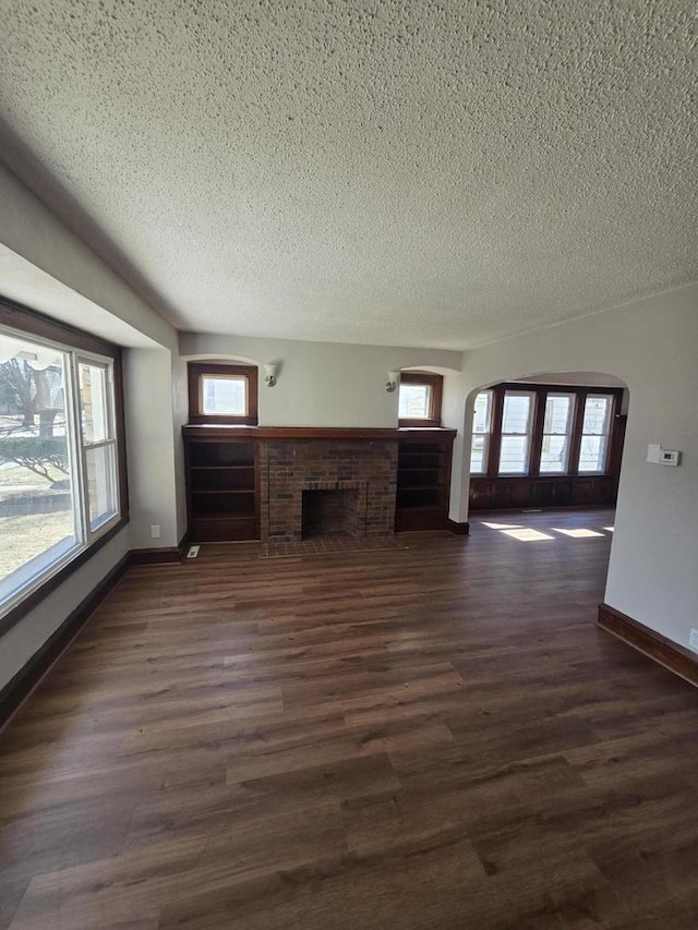 unfurnished living room featuring plenty of natural light, dark wood finished floors, a textured ceiling, and a fireplace
