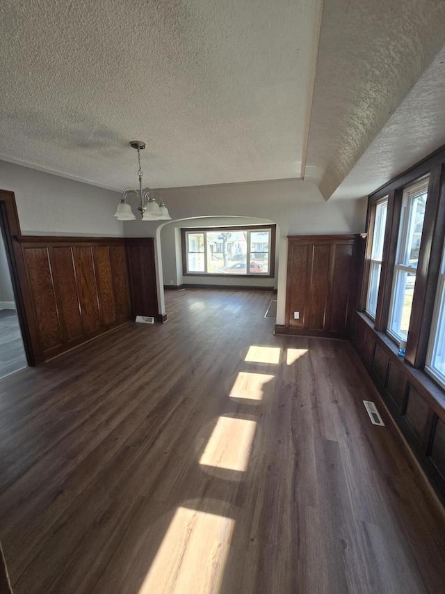 unfurnished dining area with an inviting chandelier, visible vents, a textured ceiling, and dark wood-style flooring