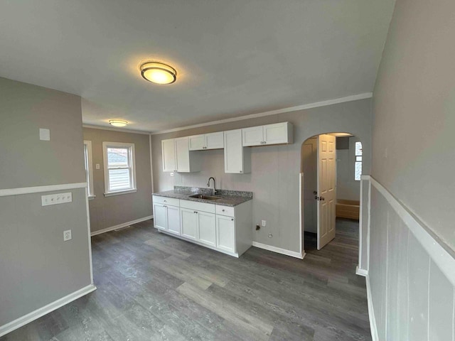 kitchen featuring arched walkways, dark wood finished floors, white cabinetry, and a sink