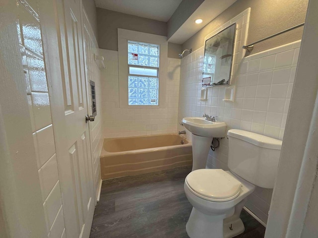 bathroom featuring wood finished floors, toilet, a sink, tile walls, and  shower combination