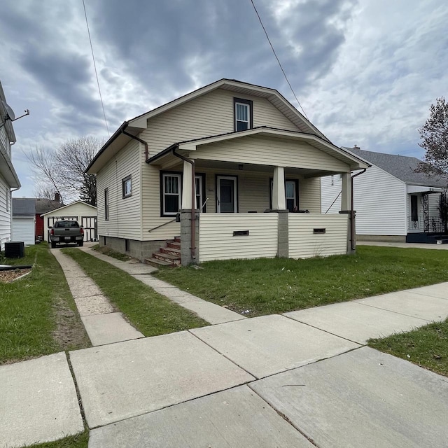 bungalow featuring central AC unit, a detached garage, covered porch, an outdoor structure, and a front yard