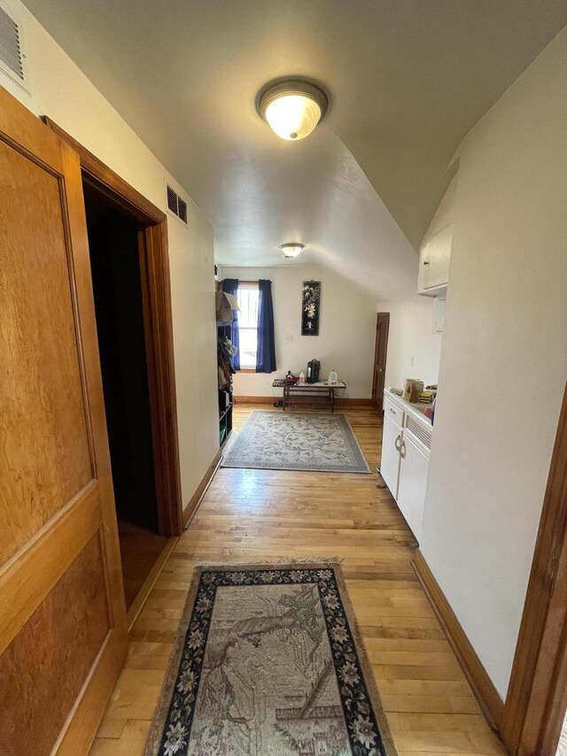 hallway featuring vaulted ceiling, visible vents, light wood finished floors, and baseboards