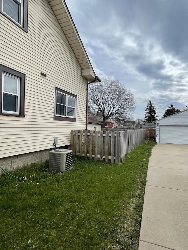 view of side of home with an outdoor structure, a lawn, central AC unit, and fence