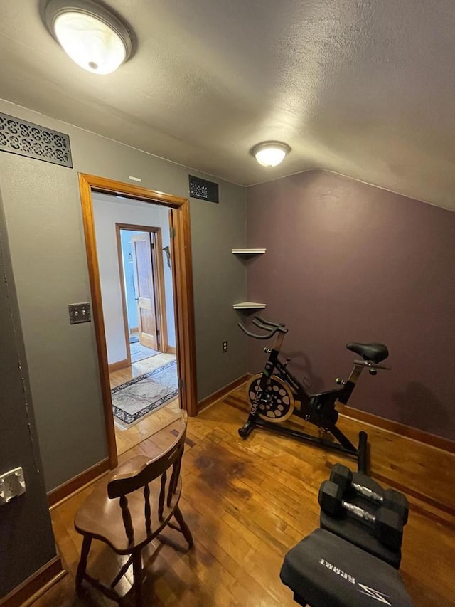 workout area with vaulted ceiling, wood finished floors, visible vents, baseboards, and a textured ceiling