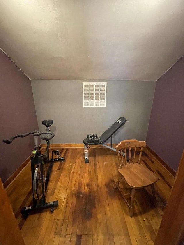 workout room with vaulted ceiling, hardwood / wood-style floors, visible vents, and baseboards