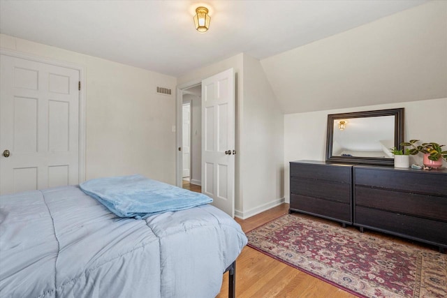 bedroom with vaulted ceiling, wood finished floors, visible vents, and baseboards