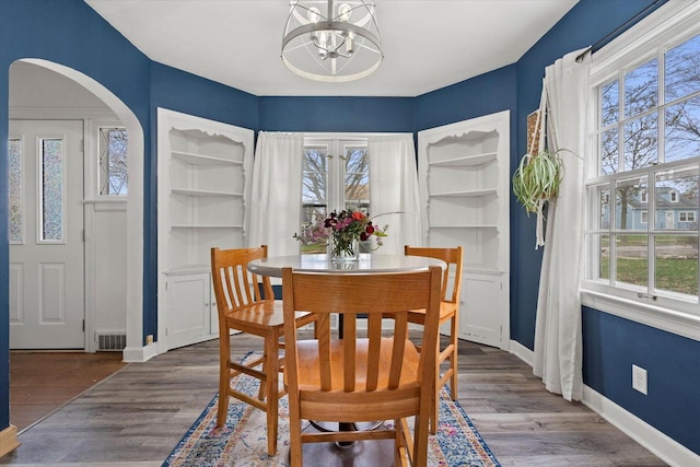 dining room with arched walkways, an inviting chandelier, wood finished floors, and plenty of natural light