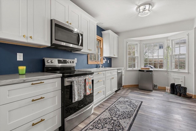 kitchen featuring white cabinets, stainless steel appliances, a sink, light wood-style floors, and baseboards