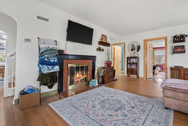 living room featuring wood finished floors, visible vents, arched walkways, baseboards, and a fireplace