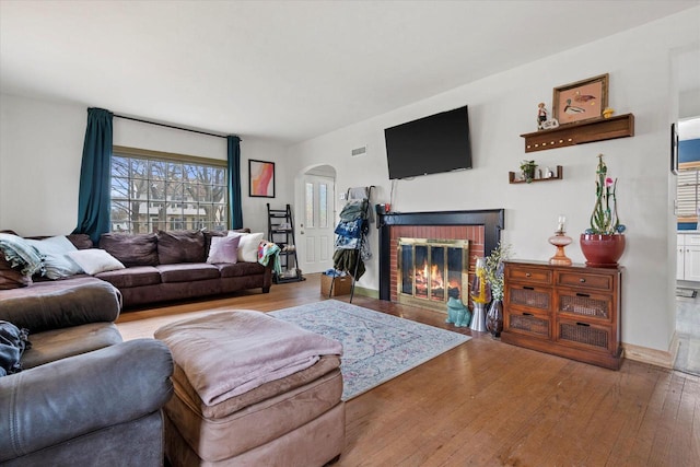 living room with arched walkways, hardwood / wood-style floors, a fireplace, and visible vents