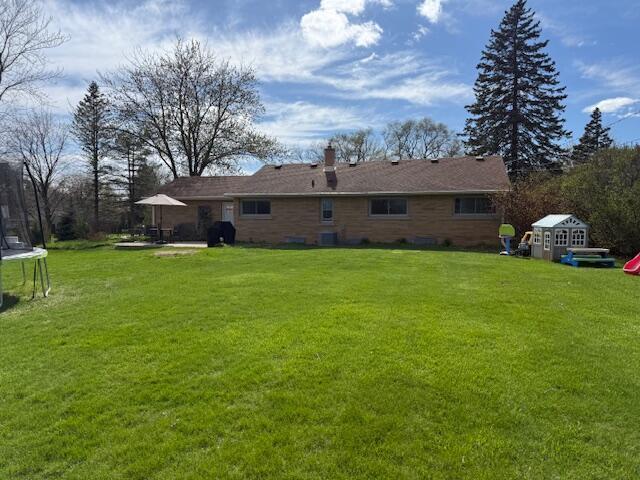 rear view of property featuring a trampoline, a chimney, a yard, and a patio