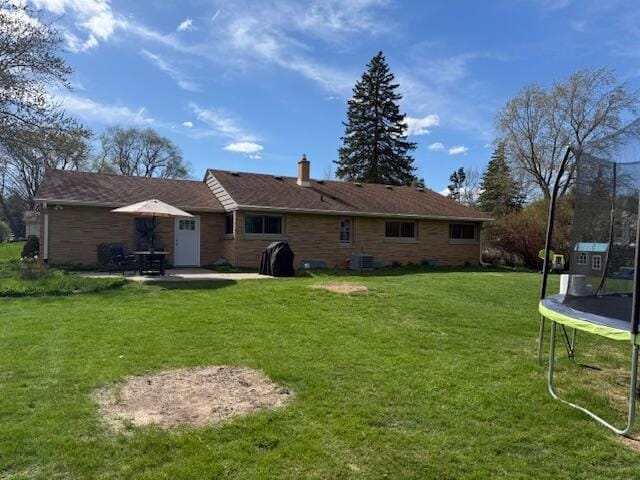 back of property featuring a patio, a chimney, central AC unit, a lawn, and a trampoline