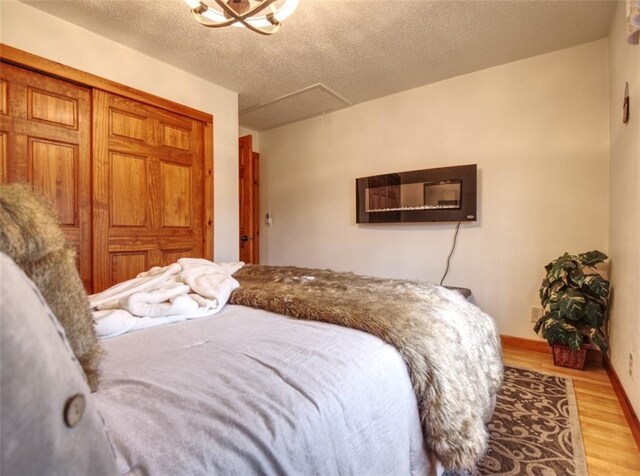 bedroom with attic access, a textured ceiling, wood finished floors, baseboards, and a closet
