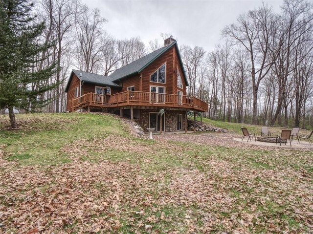 rear view of property featuring a yard, a deck, a chimney, and an outdoor fire pit