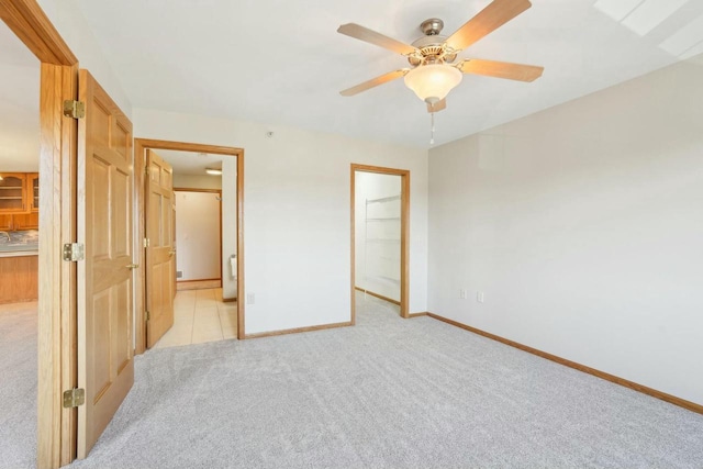 unfurnished bedroom with a walk in closet, connected bathroom, ceiling fan, light colored carpet, and baseboards