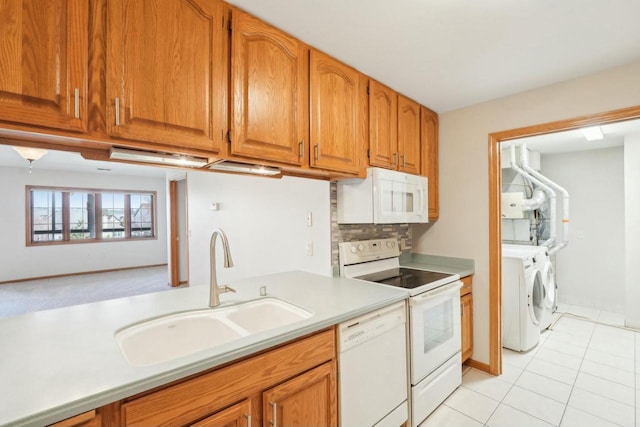 kitchen with light countertops, a sink, white appliances, washing machine and clothes dryer, and brown cabinetry