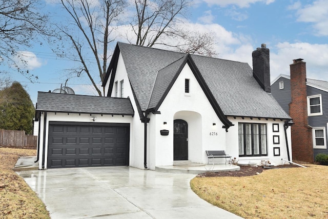 6216 N Santa Monica Blvd, Whitefish Bay, WI 53217 - tudor home featuring a front lawn, driveway, an attached garage, stucco siding, and roof with shingles