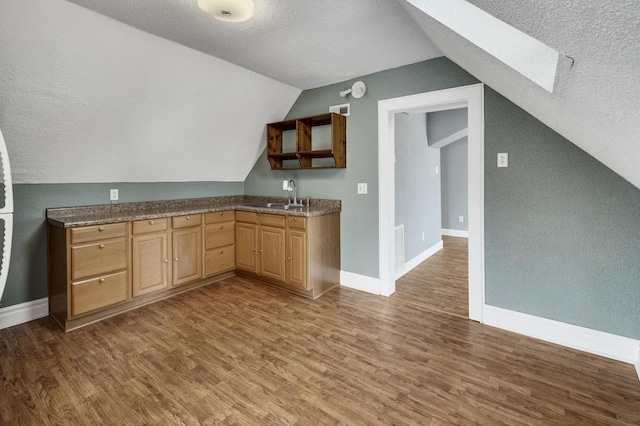 kitchen with wood finished floors, a textured ceiling, lofted ceiling with skylight, a sink, and baseboards