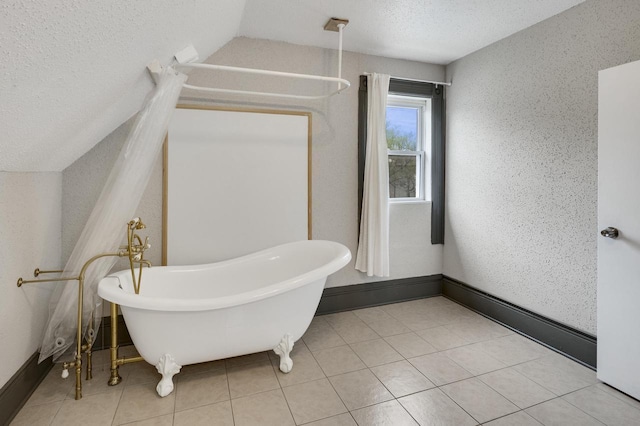 bathroom with a freestanding bath, baseboards, lofted ceiling, and a textured ceiling